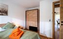 A modern bedroom with a cozy bed and fresh towels. The space is bright and welcoming, featuring a wooden closet and a view of the adjoining room.
