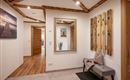 A modern hallway with wooden details and a large mirror. Wooden strips hang on the wall, and a side chair provides additional comfort.