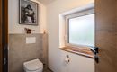 A modern bathroom with a toilet and a window. On the wall hangs a poster-like picture of a person on the toilet.