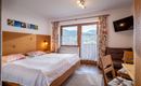 A cozy hotel room with two beds and wooden decor. Large windows provide a view of the mountains and ensure plenty of daylight.