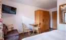 A cozy room with a bed, a table, and two chairs. On the wall hangs a television, and there is a wooden wardrobe.