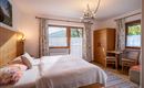 A cozy bedroom with a double bed and wooden furniture. Large windows let in plenty of daylight and offer a beautiful view outside.