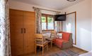 A bright room with wooden furniture and a small dining area. There is a television and large windows with curtains.