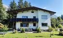 Ein modernes Haus mit Solarpanelen und einem gepflegten Garten. Umgeben von Bäumen und Bergen, bietet es eine schöne Aussicht.