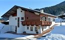 A beautiful chalet in the snow with a wooden balcony. In the background, snow-covered mountains can be seen.