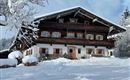 A traditional wooden house in the snow, surrounded by a wintry landscape. The sky is partially cloudy and the surroundings are quiet and peaceful.
