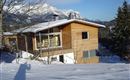 A modern wooden house in the snow, surrounded by mountains. The clear sky and the snow-covered landscape create a peaceful winter atmosphere.