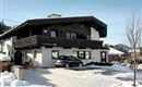 A cozy, multi-story house in the snow with a car in front. Snow-covered mountains are visible in the background.