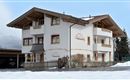 A beautiful building in Alpine style, surrounded by snow. The facade is bright with wooden decorations and classic windows.