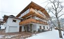 Ein modernes Haus im Schnee mit einem großen Balkon aus Holz. Die Umgebung ist ruhig und malerisch, ideal für einen Winteraufenthalt.