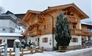 Een mooi houten huis in alpine stijl met meerdere balkons. Er ligt sneeuw rondom en de sfeer is gezellig.