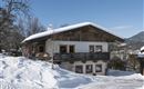 A traditional wooden house in the snow with a beautiful balcony. The sky is clear and blue, surrounded by a winter landscape.