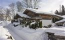 A cozy wooden house in the snow, surrounded by trees. The landscape is wintry and peaceful.