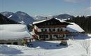 Ein gemütliches Chalet in einer verschneiten Berglandschaft. Die Umgebung ist mit frischem Schnee bedeckt und die Berge sind klar sichtbar.