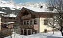 A charming house covered in snow in winter. Majestic mountains can be seen in the background.