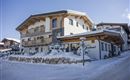 A cozy chalet in the snow, surrounded by trees. The sky is clear and the architecture is rustic.