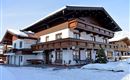A traditional house in alpine style, surrounded by snow. The facade is adorned with wooden decorations and a balcony.