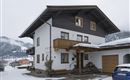 A beautiful house in the Alps, surrounded by snow-capped mountains. The facade is white with a wooden balcony.