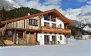 Ein charmantes Chalet in den Bergen, umgeben von Schnee. Die Fassade kombiniert Holz und weiße Wände, mit Blick auf die beeindruckenden Berge.