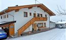 Ein gemütliches Haus im Schnee mit einem Holzbalcony. Die Umgebung ist winterlich und ruhig.