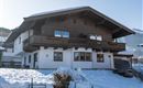 A cozy house in alpine style with wooden cladding. The snow covers the ground and the surroundings are mountainous.