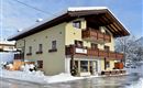 A beautiful building in the mountains, surrounded by snow. It has a traditional style with wooden balconies and a clear blue sky.