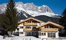 A beautiful chalet in the snow with impressive mountains in the background. The clear blue sky provides a picturesque alpine setting.