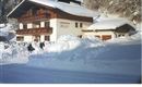 A cozy chalet in the snow, surrounded by snow-covered trees. The sky is clear and the landscape looks wintery and idyllic.