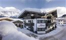 A cozy holiday home in the snow with mountains in the background. The surroundings are wintry and inviting.