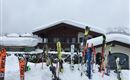 A chalet in the snow with many skis in front of the door. The sky is cloudy and the surroundings are wintry.