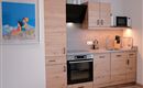 A modern kitchen with wooden cabinets, a stove, and a microwave. A colorful picture of "Heidi" hangs on the wall.