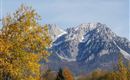 A majestic mountain with a snow-capped peak and colorful foliage in the foreground. The sky is clear, and it is a beautiful autumn day.