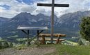 A view of the mountains with a wooden cross in the foreground. A bench-table combination invites you to linger.