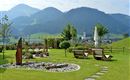 Gartenanlage des Hotel Alpenpanorama in der Ferienregion Wilder Kaiser mit Sonnenliegen, Rundbank und Panoramablick auf die Tiroler Berge.