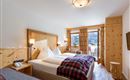 Gemütliches Doppelzimmer im Hotel Alpenpanorama in der Ferienregion Wilder Kaiser mit Holzbett, kariertem Plaid und Fensterblick in die Berge.
