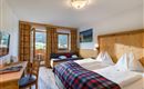 Gemütliches Doppelzimmer mit Holzmöbeln, karierten Details und Balkon mit Bergblick.