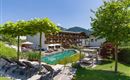 Außenansicht des Hotels Alpenpanorama mit Garten, Pool, Sonnenliegen und Blick auf die Tiroler Bergwelt.