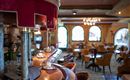 Eine gemütliche Innenansicht eines Restaurants mit einer Bar und Sitzplätzen. Die Fenster lassen natürliches Licht herein und schaffen eine einladende Atmosphäre.
