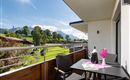 Ein schöner Balkon mit Blick auf grüne Wiesen und Berge. Ein Tisch mit Blumen und einer Flasche Wein lädt zum Entspannen ein.