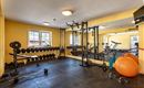 Ein modernes Fitnessstudio mit Gewichten und Trainingsgeräten. Die Wände sind gelb gestrichen und es gibt große Spiegel sowie einige Fitnessbälle.