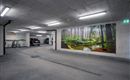 Eine moderne Tiefgarage mit einem großen Wandbild eines Waldes. Im Hintergrund stehen mehrere Fahrzeuge und Fahrräder sind abgestellt.