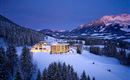 Ein modernes Hotel in einer schneebedeckten Landschaft bei Dämmerung. Im Hintergrund sind majestätische Berge und eine ruhige Winteratmosphäre zu sehen.