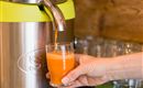 Een drankdispenser met verse, oranje sap wordt in een glas gegoten. Een hand houdt het glas vast terwijl het sap wordt ingeschonken.