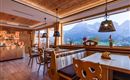 Een gezellig restaurant met houten interieur en grote ramen. Op de achtergrond zijn indrukwekkende berglandschappen te zien.