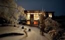 Ein modernes Haus im Schnee bei Nacht, beleuchtet von warmem Licht. Der Garten ist mit schneebedeckten Bäumen geschmückt.