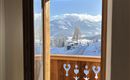 An open window with a view of snow-covered mountains and a wooden balcony. The view is clear and sunny.