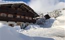 A cozy wooden house in a snowy landscape. The snow is high and the sky is clear and blue.