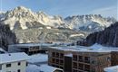 A winter landscape with snow-covered mountains and modern buildings. The surroundings are quiet and picturesque, surrounded by spruce forest.