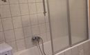 Een eenvoudige badkamer met een bad en een eigen douchewand. Aan de linkerkant staat een wasmachine.