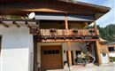 A traditional wooden house with a balcony and blooming plants. The facade is bright and welcoming, surrounded by a picturesque landscape.